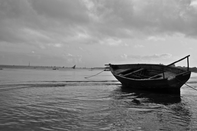 Black and white stock photo of a boat docked at the beach with water around it