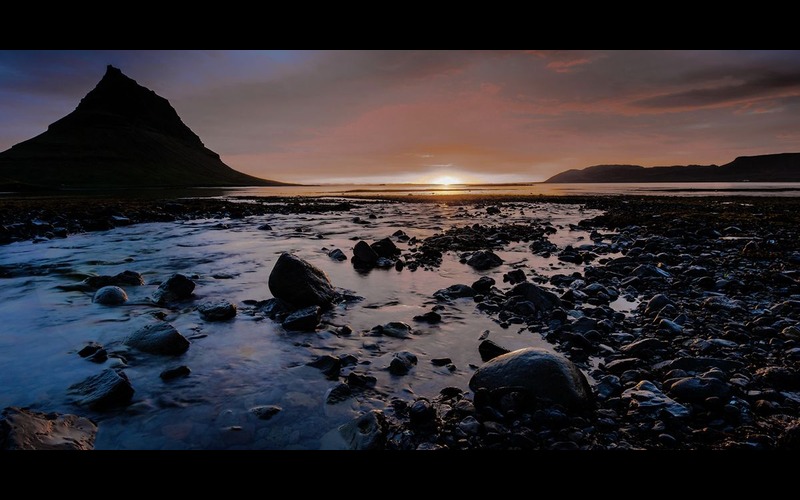 A scenery of sunrise with mountains and a water body
