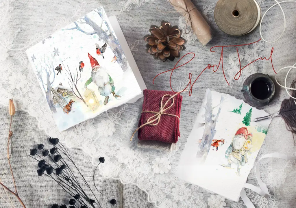 A flat lay shows two different cards with watercolor gnome designs on a white textured fabric.